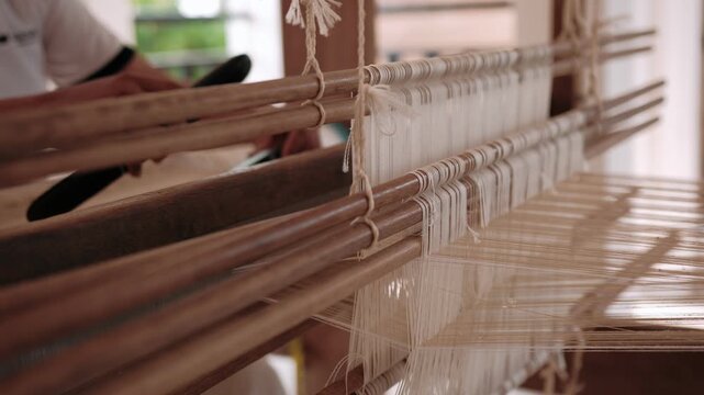 Woman weaving silk fabric on a traditional handloom using ancient weaving techniques, surrounded by nature, Cambodia, Siem Reap.