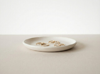 Minimalist matte white ceramic jewelry tray holding small delicate gold rings on a neutral beige background