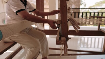 Woman weaving silk fabric on a traditional handloom using ancient weaving techniques, surrounded by nature, Cambodia, Siem Reap.