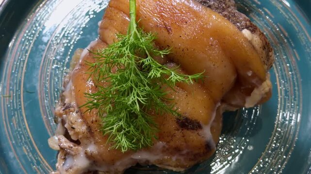 Roasted pork knuckle on a plate garnished with fresh dill.