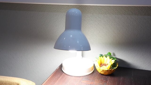 Smart small metal smart lamp on a bedside table illuminating a decorative sunflower, modern home decor ambient lighting concept.