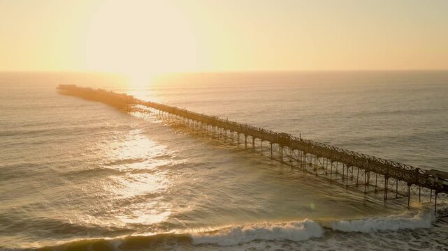 Sunset beach scene in Pimentel, Peru, with warm golden light, gentle waves and swimmers enjoying the ocean near the iconic pier. Perfect for travel and summer tourism content
