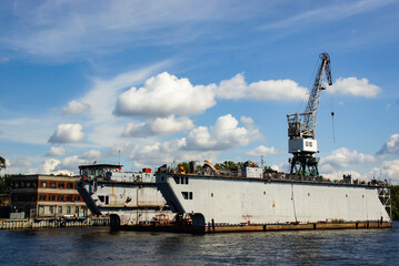 industrial floating dock is moored alongside riverbank. The vessel with a crane for heavy lifting and loading operations. for maritime-themed content, or articles about river transport infrastructure.