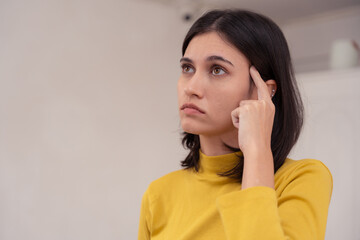 Young woman pointing at her temple and looking confused, indicating memory problems or difficulty concentrating. memory, forget, thinking, mind, brain, confused, confusion, woman, forgetful, problem.
