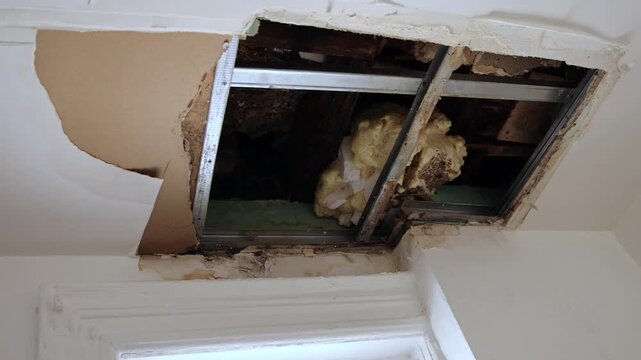 hole in broken ceiling with insulation and old construction sheetrock showing through sheet rock exposed repair water damage bathroom cut out wall repairing damaged