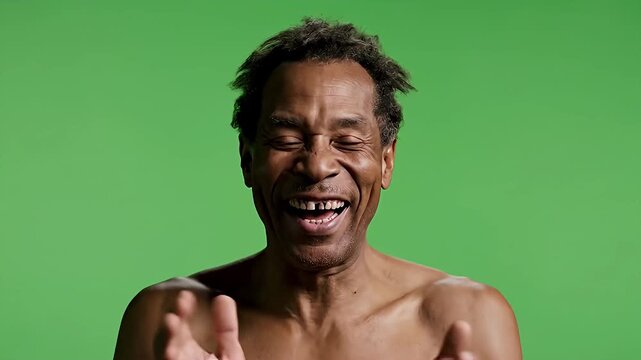 Mature African American man with a genuine hearty laugh eyes closed in amusement showing missing teeth on a bright green screen Expressing pure joy and happines