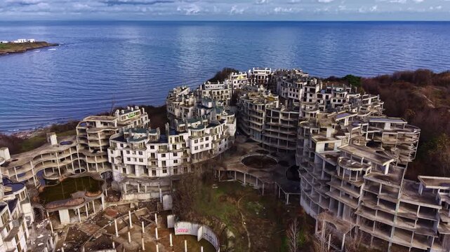 Overlooking the calm sea, an abandoned resort reveals its deteriorating structures, once vibrant and full of life, now silent testaments to faded ambitions and nature reclaiming its space.