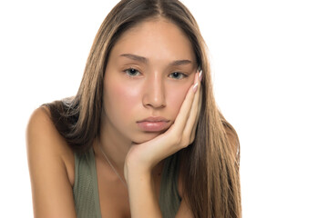 Naklejka premium Studio shot of young woman with long brown hair wearing green tank top, resting her face on hand and looking bored, on white background.