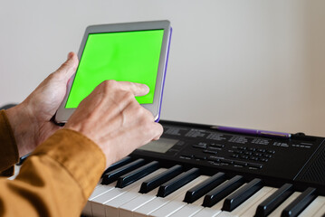 Male pianist using tablet with mobile apps for self study, closeup photo. Using green screen tablet over piano keyboard for digital music concept