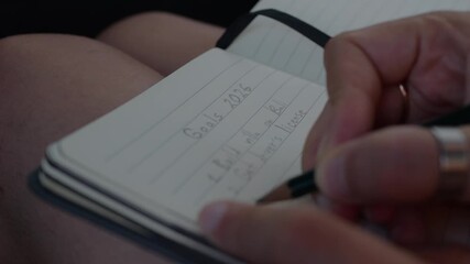 New Year, New Goals. Close-up of a hand writing a 2026 personal goals list with a pencil in a lined notebook, focusing on detail and handwriting. 4K
