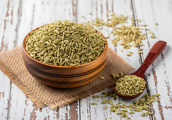 Dried fennel seeds in a wooden bowl and spoon on rustic wooden background