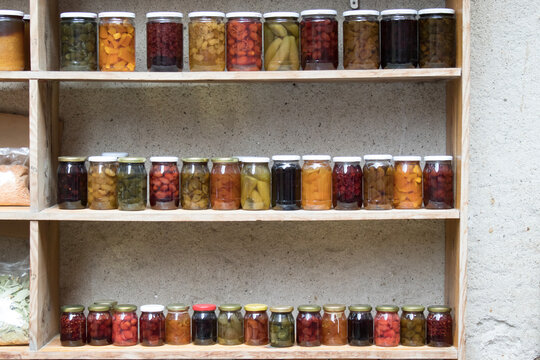 Rows of glass jars with jams, pickles and compotes on wooden shelves; homemade preserves pantry concept, colorful food background. - Powered by Adobe