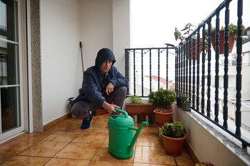 Obraz premium Man on Balcony Watering Plants With Green Can Amid Potted Garden