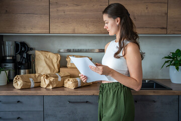 Young woman reviewing a receipt while checking delivered meal kit ingredients on her kitchen...