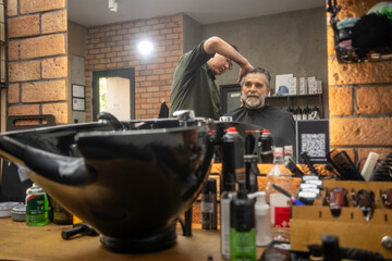 Barber cutting hair of mature man with reflection in mirror at salon