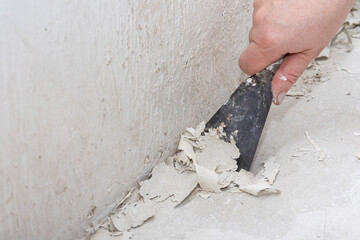 Hand Removing Old Paint from Wall with Scraper Tool.