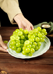 Fresh Green Seedless Grapes in Hands on Wooden Table