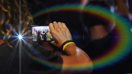 Man holding phone recording concert, capturing band and crowd while lights creating flash and rings