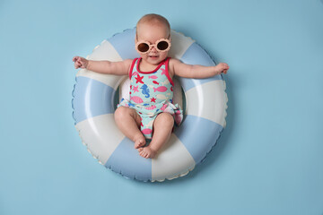 Naklejka premium Cute little baby with sunglasses on inflatable ring against light blue background, top view