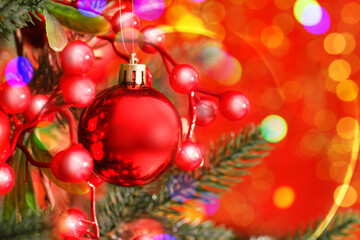 Merry Christmas and Happy Winter Holidays greeting card. Fir tree with festive ball and bokeh lights on red background