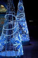 LED snowflake decorations glow in cool blue and white tones. Festive holiday structures sparkle against a dark night background.