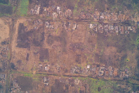 Aerial top down view of destroyed village ruins with roofless foundations. War zone settlement destruction and scorched earth landscape background.