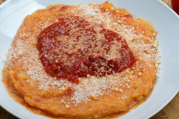 Top view flat lay of traditional Italian polenta with tomato sauce and cheese surrounded by raw ingredients on a wooden table