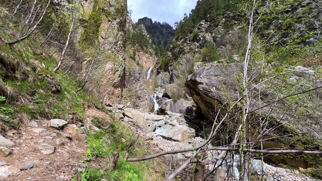 Shagatsikomdon Waterfall, in the spring in the Caucasus Mountains. Mountain landscape. Waterfall in the Tsey Gorge. North Ossetia-Alania, Russia. A multi-stage 15-meter waterfall in the sunlight. 4К