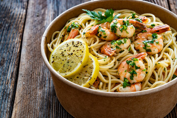 Takeaway food - fried shrimps with noodles and lemon in lunch box to go on wooden table
