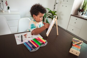Toddler drawing on easel with colorful markers at home