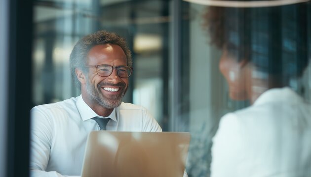 Ecstatic Entrepreneur Engaged In Laptop Work And Discussing With African American Female Co-Worker In Corporate Office. Windowed Perspective.