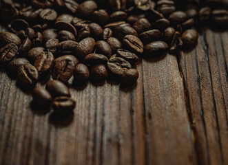 Roasted arabica coffee beans scattered on a rustic dark wooden table, creating a rich brown aroma background