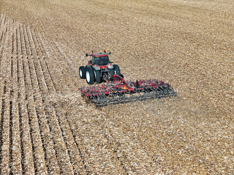 Red farm tractor pulling a tillage implement to shred corn stalks for the purpose of residue managment