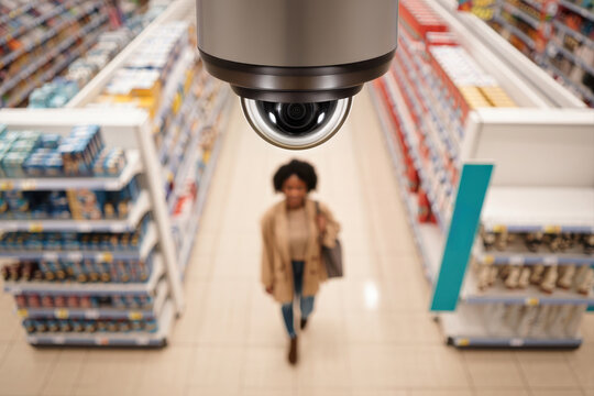 Overhead security camera monitoring blurred shopper in supermarket aisle.