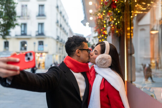 Couple kissing and taking a selfie on a city street, celebrating christmas and winter holidays in madrid