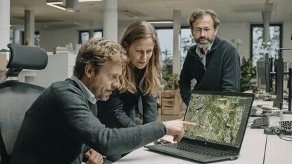 Medium shot of consultant discussing climate resilience strategies with team using satellite imagery to mitigate investment losses from extreme weather fluctuations