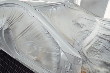 Professional car painting in a specialized spray booth at an auto service center. Body repair and surface preparation process. Quality maintenance and technical service for modern vehicle transport.