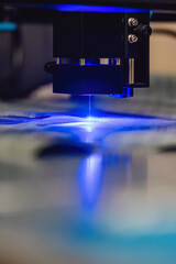 Close up of laser cutting paronite. Powerful blue laser burning complex gasket shape out of asbestos material. Smoke and sparks visible during precise manufacturing of industrial seals.