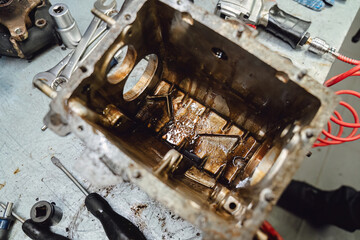 Oily transmission details: broken gearbox unit and green bin with spare parts. Close up of worn out mechanism before overhaul or recycling. Industrial grunge texture and mechanical defects.