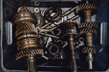 Oily transmission details: broken gearbox unit and green bin with spare parts. Close up of worn out mechanism before overhaul or recycling. Industrial grunge texture and mechanical defects.