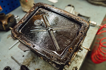 Old dirty car gearbox transmission on workbench in auto service garage. Disassembled mechanical transmission unit with oil and rust. Auto repair and spare parts replacement concept for restoration.