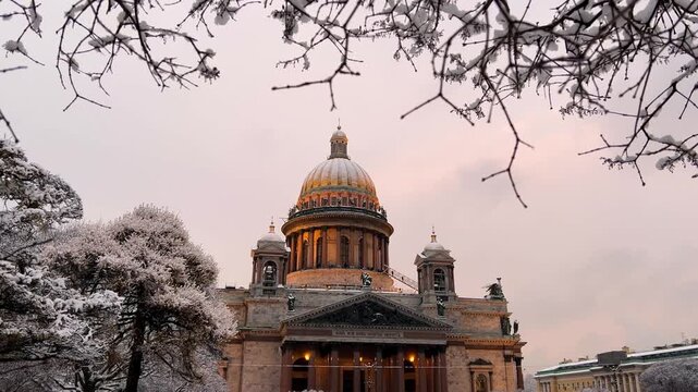 St. Petersburg, Russia - November 23, 2025: View of the snow-covered St. Isaac's Square with snow-covered trees and St. Isaac's Cathedral on a winter day at sunset. 4K