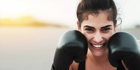 Determined young woman wearing boxing gloves smiling at camera, showing confidence and power in a boxing workout