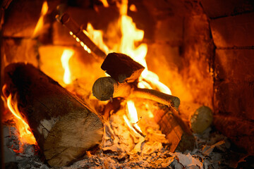Wood logs burning with bright orange flames in a brick fireplace, casting warm, cozy light and glowing embers that create comfort and heat on a cold evening
