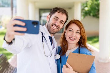 Doctor and nurse medical team taking selfie with phone, smiling and enjoying break outside hospital