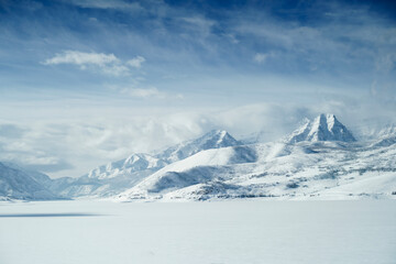 The Wasatch Back Mountains in Heber City Utah over a frozen lake with clouds and snow over mountains and blue sky