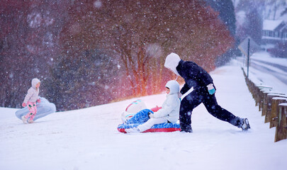Happy Children Sledding Down a Snowy Hill &ndash; Winter Fun in Motion under Soft Falling Snow. Active Family Snow Day