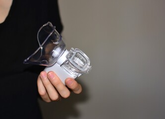 Hand holding a portable nebulizer device for respiratory treatment. Symbol of asthma care, inhalation therapy, lung disease management and home medical support.