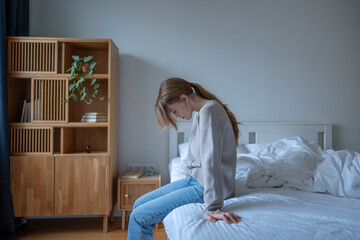 Exhausted stressed woman sits in bedroom hanging head in helplessness feels mental pressure, uncertainty. Tired anxious female alone at home overwhelmed worried by thoughts. Depression, inner tension