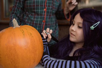 Girl draws eyes and mouth on pumpkin to carve jack-o'-lantern for Halloween